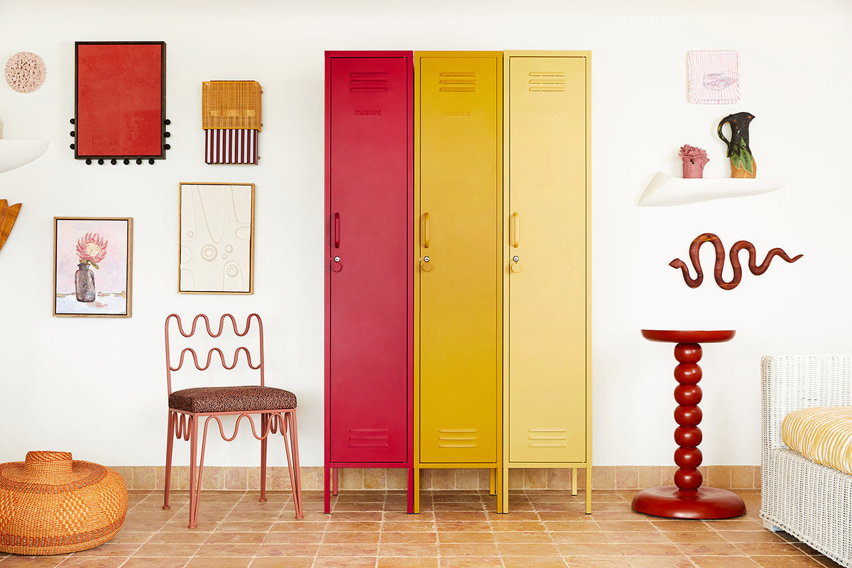 Gli armadietti “ Skinny ” nei colori Poppy, “ Mustard ” e Butter sono allineati lungo una parete della galleria, insieme a una sedia ondulata e a un tavolino