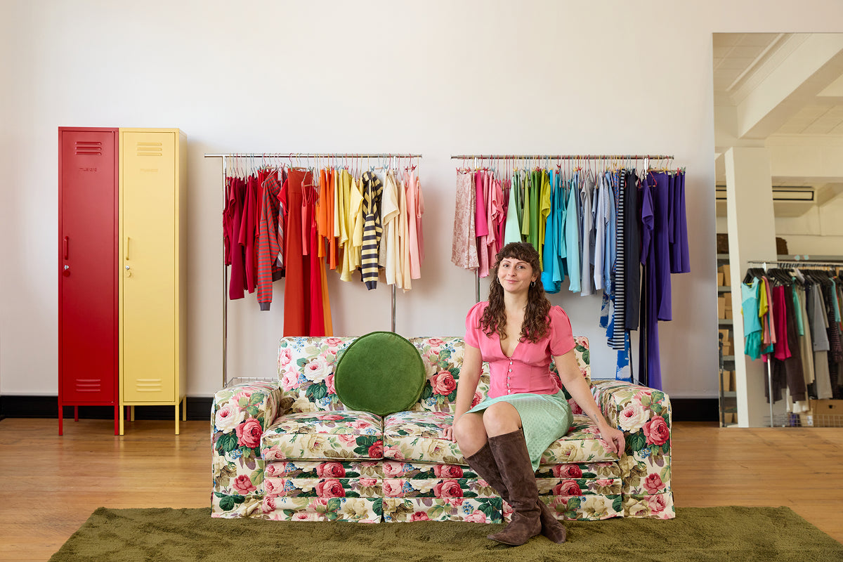 Die „ Skinny “-Spinde in Poppy-Rot und Buttergelb neben den nach Regenbogenfarben sortierten Kleiderständern im Olga-Joan-Modestudio; die Gründerin sitzt auf einem Sofa mit Blumenmuster