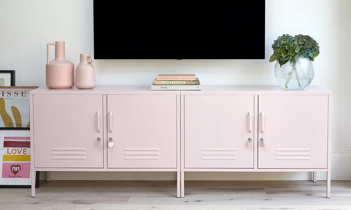Zwei „The Lowdown in zartem Blush-Rosa unter einem an der Wand montierten Fernseher, dekoriert mit Vasen, Büchern und einer Blattpflanze