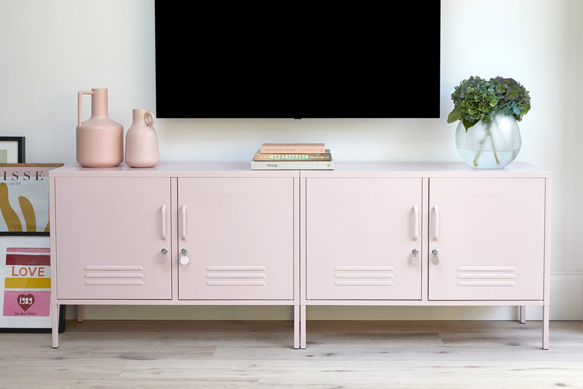 Deux Lowdown « The Lowdown » de couleur rose pâle « Blush », placés sous une télévision murale, agrémentés de vases, de livres et d'une plante à feuillage luxuriant