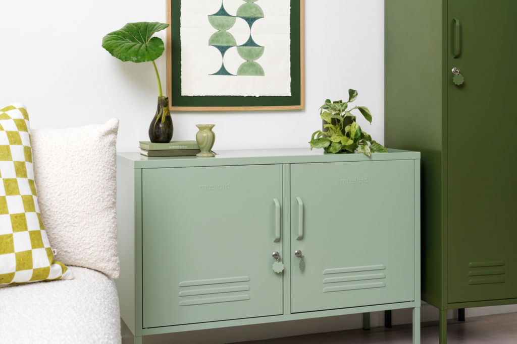 A Sage Lowdown sits next to an Olive Skinny locker. They are accessorised with leafy green plants, some green books and an artwork in shades of green.