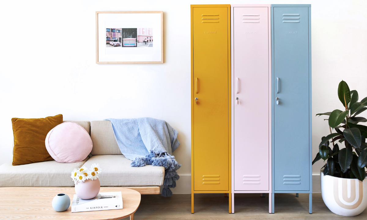 Drei Mustard Made Skinny "-Schränke stehen nebeneinander. Von links ist der erste Mustard, dann Blush und dann Ocean. Auf der linken Seite steht ein Sofa mit einem Holzrahmen und beigen Polstern, auf denen Kissen in verschiedenen Formen und Farben liegen. 