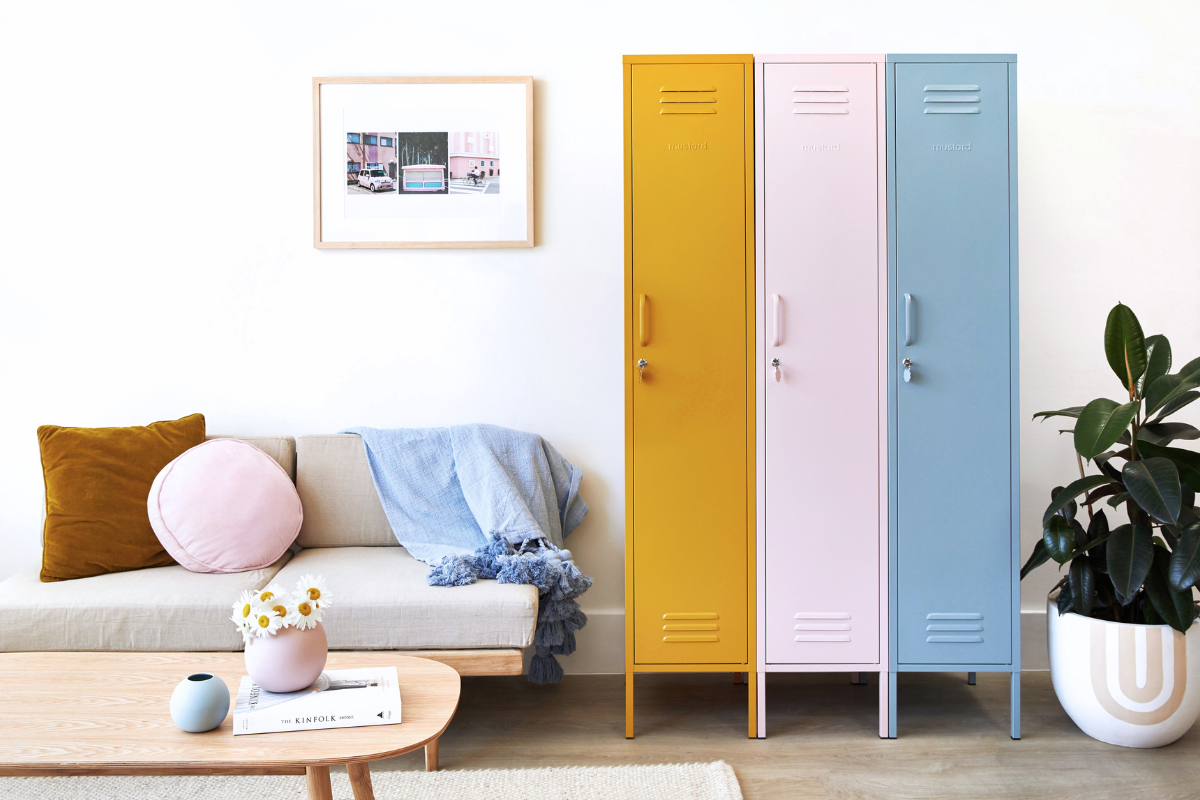 Drei Mustard Made Skinny "-Schränke stehen nebeneinander. Von links ist der erste Mustard, dann Blush und dann Ocean. Auf der linken Seite steht ein Sofa mit einem Holzrahmen und beigen Polstern, auf denen Kissen in verschiedenen Formen und Farben liegen. 