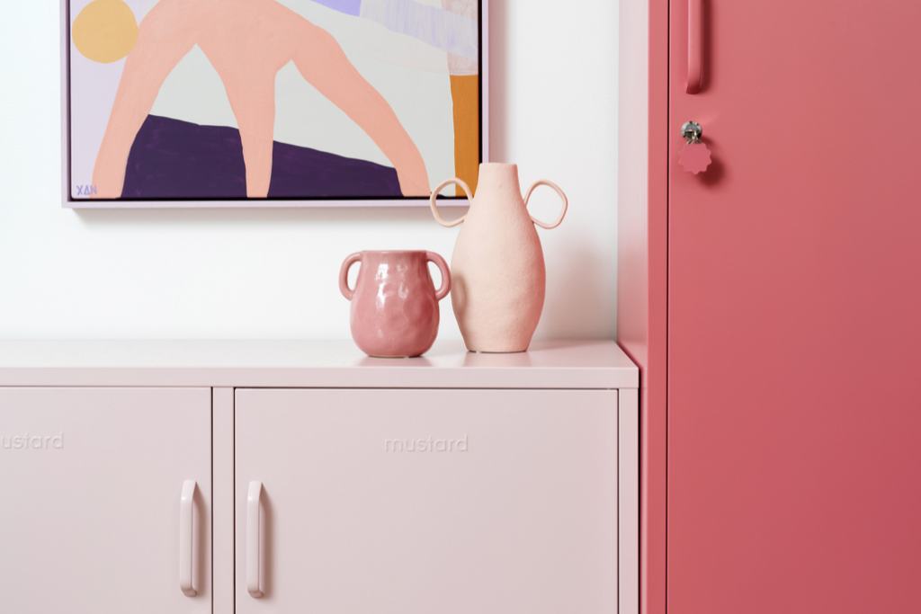 A Berry Skinny stands next to a Blush Lowdown with two pale pink vases on top. There is an abstract painting hanging on the wall in shades of pink and purple.