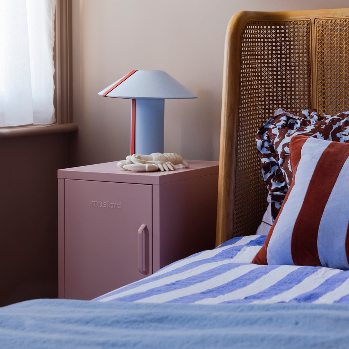 The Shorty bedside locker in Blush pink beside a cane bed with striped bedding