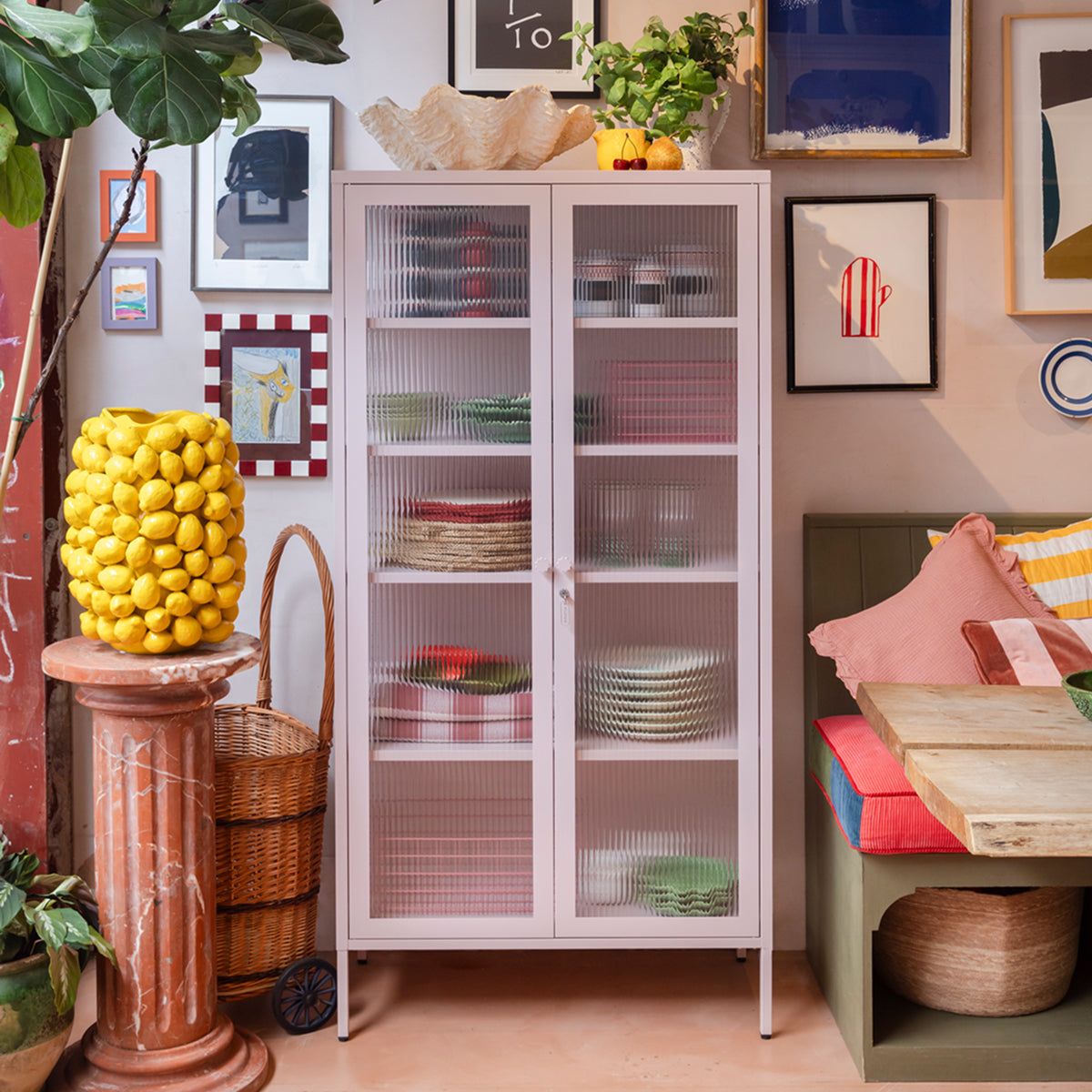The Collector glass display cabinet in Blush pink holding plates beside a dining nook
