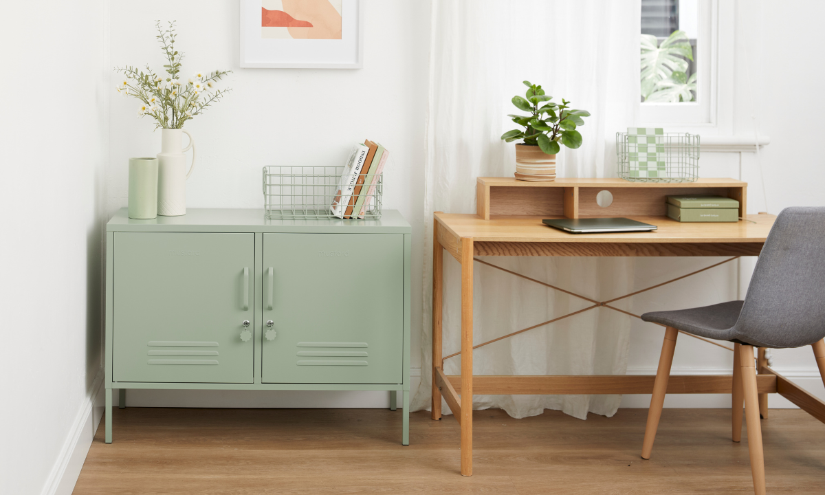 Una taquilla de Sage Lowdown está sentada en un despacho casero junto a un escritorio de madera con una silla. Hay un portátil sobre el escritorio y pequeñas plantas en macetas y libros decorando el espacio.