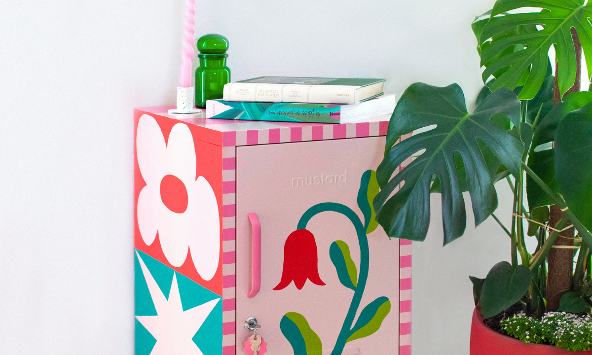 Un Shorty Blush a été peint avec un motif floral détaillé, avec les bords en damier rose. Il est flanqué d'un plant de monstera dans un pot rouge.