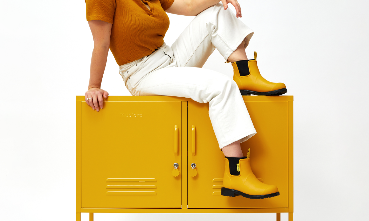 Becca seduta in cima a The Lowdown Locker in Mustard, con gli stivali Merry People.